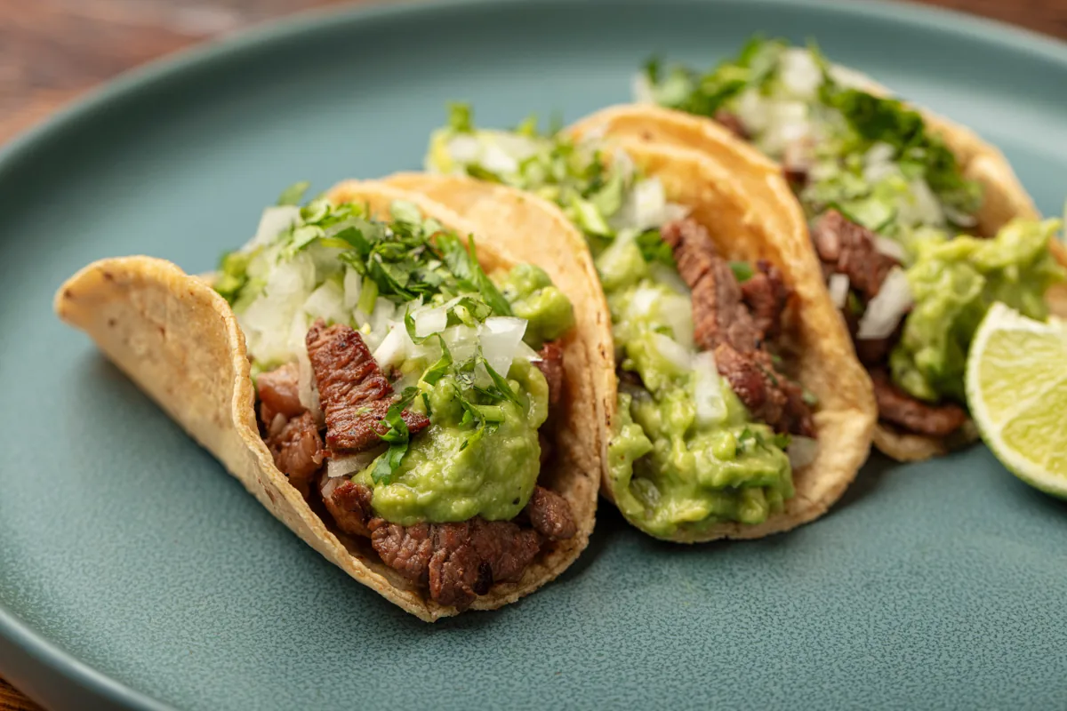 Steak tacos with guacamole, onion, cilantro and lime on a green plate